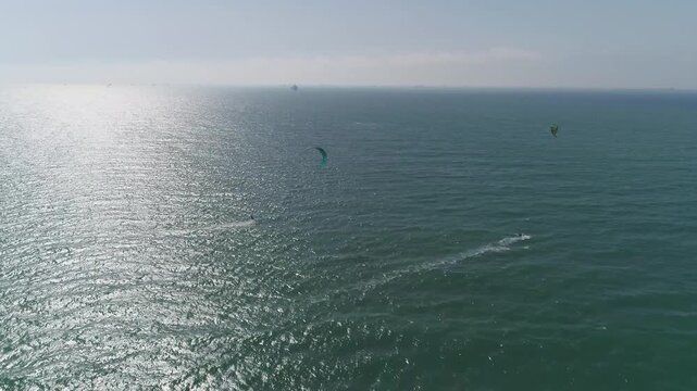 Aerial drone view of kitesurfers riding waves in the open sea under sunlight