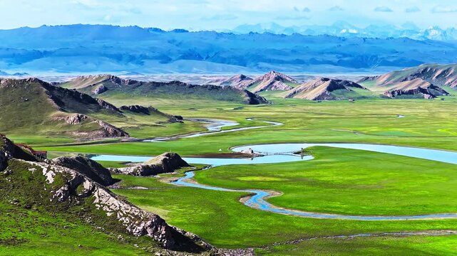 Aerial view of a meandering river flowing through lush green meadows in Bayinbuluke Grassland, Xinjiang, China