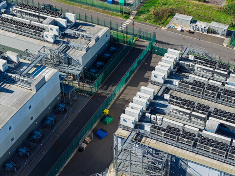 Aerial view of a modern data center facility featuring rows of industrial cooling units on rooftops, secure perimeter fencing, and paved access paths, United Kingdom.