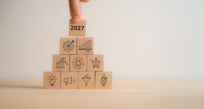 2027 Business Strategy. Marketing Planning, Growth Roadmap. Placing a 2027 wooden block atop a pyramid of marketing, sales, growth, target icons. Business strategy, digital marketing, future success.