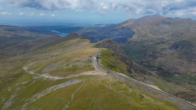 Aerial view of the Snowdon Mountain Railway winding through the rugged mountain landscape with hikers walking along the path in Llanberis, Wales, United Kingdom.