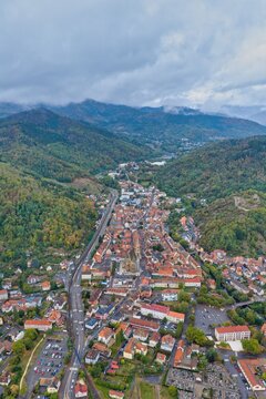 Aerial view of the historic town of Thann featuring the Collegiate Church of Saint-Thiebaut, surrounded by green hills, winding roads, and residential rooftops in Thann, Grand Est, France.