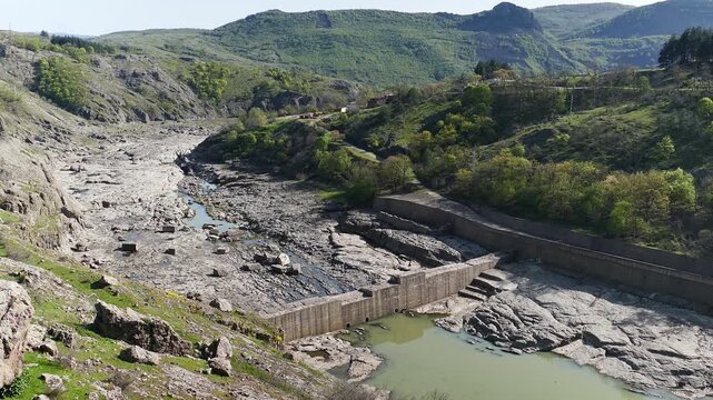High angle landscape view of the dry Arda riverbed below Studen Kladenets dam. Aerial perspective of a rocky river canyon with low water levels and a concrete weir in Eastern Rhodopes, Bulgaria.