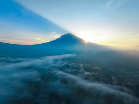 Aerial view of the sunrise over Mount Sindoro with thick morning mist covering the valley in Selomerto, Central Java, Indonesia.