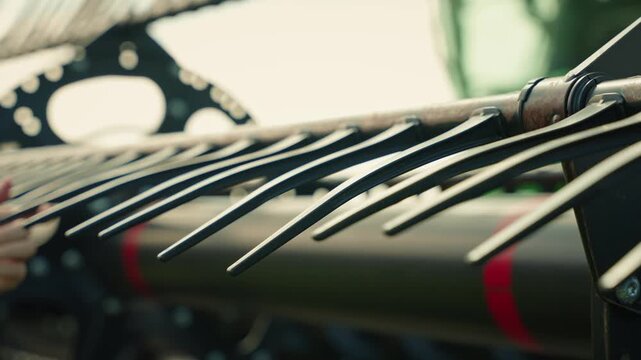 Static slow motion close-up of plastic tines on a combine header as a farmer runs a hand down the row, checking each tine before harvest