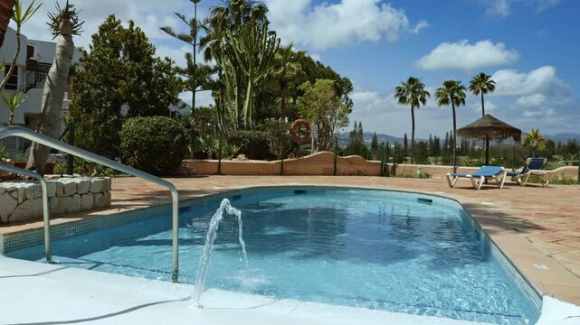 Exotic luxury resort, outdoor hotel pool deck with fountain, palm trees, cacti, and lounge chairs, Mijas, Malaga, Spain