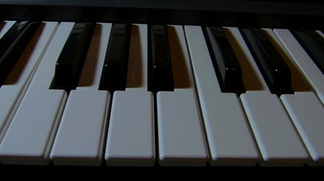 Slider tracking shot along a piano keyboard under dim atmospheric lighting. Close up creative view of ebony and ivory musical keys under dramatic soft illumination indoors in Bulgaria.