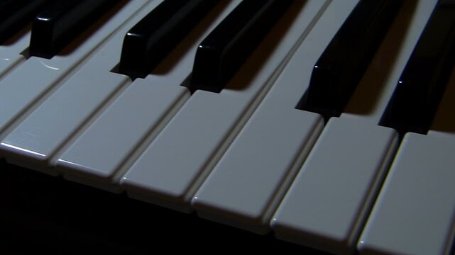 Slider tracking shot along a piano keyboard under dim atmospheric lighting. Close up creative view of ebony and ivory musical keys under dramatic soft illumination indoors in Bulgaria.