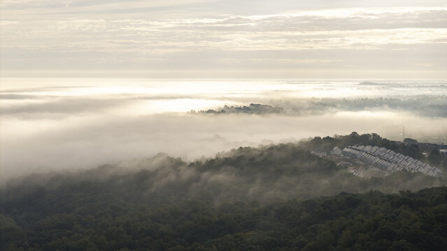 Aerial view of a mist landscape covering a dense forest and a residential area with rows of houses in Lesser Poland Voivode, Poland.