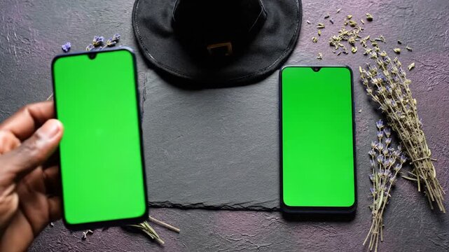 Hand Moving Green Screen Smartphone Among Witch Hat Lavender Herbs And Amber Bottles On Dark Slate Table