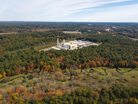 Aerial view of the ANP Bellingham Energy Project power plant surrounded by vibrant autumn forest and a winding stream in Bellingham, Massachusetts, United States.