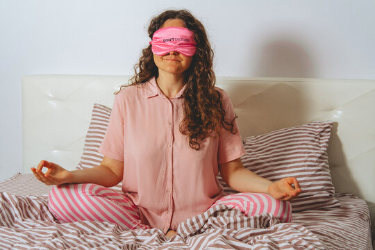 Woman wearing a sleep mask meditates on her bed in the bedroom