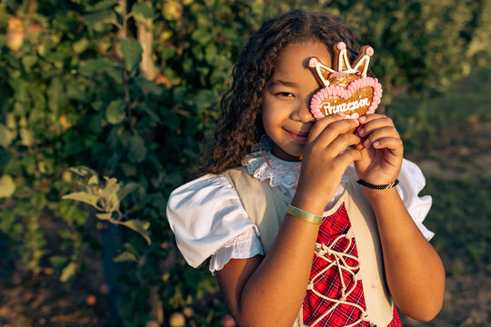 Smiling girl holds gingerbread heart in apple orchard