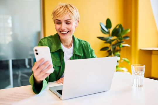 A happy businesswoman uses her smartphone at an office desk