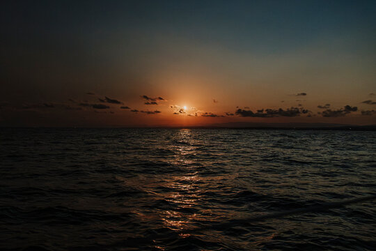 The sun sets over the dark ocean horizon during a serene evening