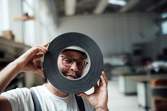 Playful carpenter looks through a tape roll in the workshop