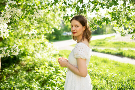 A smiling woman in a white dress enjoys an apple orchard in spring
