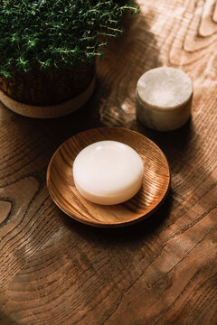 A white bar of soap sits on a wooden dish on a rustic table