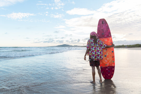 Surfer stands on the beach holding a surfboard looking at the ocean