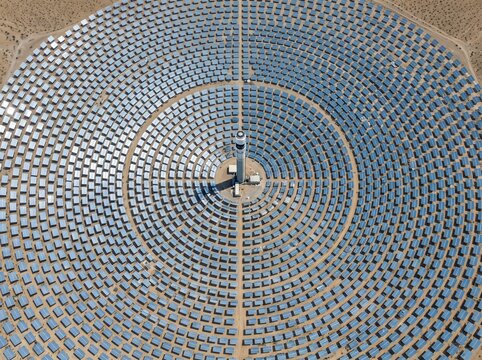 High angle aerial drone view of a massive concentrated solar power plant with concentric circles of heliostat mirrors surrounding a central receiver tower