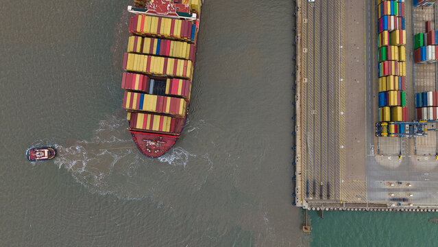 Aerial view of a large container ship being maneuvered by a tugboat at the Port of Felixstowe, with rows of colorful shipping containers in Felixstowe, England, United Kingdom.