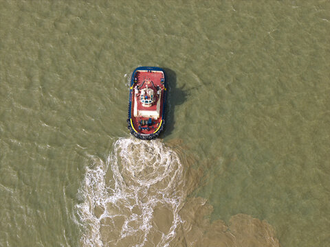 Aerial view of a tugboat navigating through the water and creating a wake near the Port of Felixstowe, Felixstowe, England, United Kingdom.
