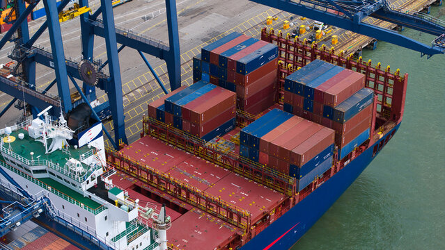Aerial view of a container ship being loaded with colorful shipping containers at the Port of Felixstowe, with industrial cranes and calm water in Felixstowe, England, United Kingdom.