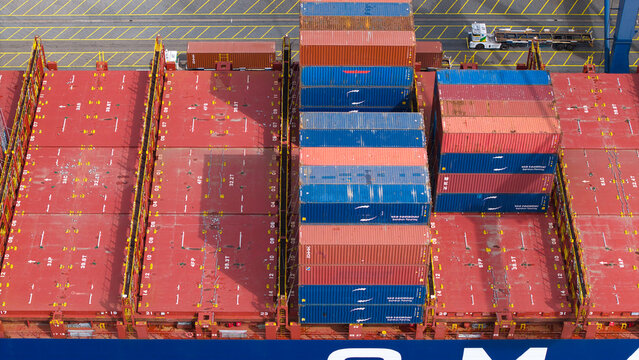Aerial view of a container ship deck loaded with stacked red, blue, and orange shipping containers at the Port of Felixstowe in Felixstowe, England, United Kingdom.