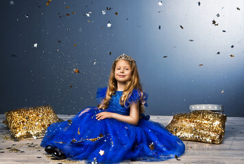 Beautiful little girl wearing luxury blue princess gown and tiara sitting with golden sequin pillows © Oleksandr