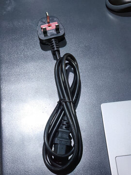 Black electric cable with plug isolated on dark background, showing power connection, electronic accessory, and household equipment concept for technology and utility use.