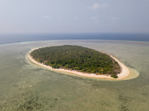 Aerial view of Cowo-Cowo Island surrounded by shallow turquoise waters, coral reefs, and dense tropical vegetation, Wakatobi, Southeast Sulawesi, Indonesia.