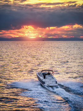 Aerial rear view of a motorboat cruising over the ocean into the golden sunset