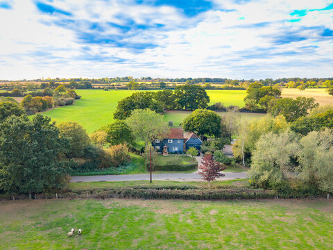 Idyllic drone view of an isolated detached home in the heart of the Essex, UK countryside. A horse paddock is to the rear and a trio of sheep are near the foreground.
