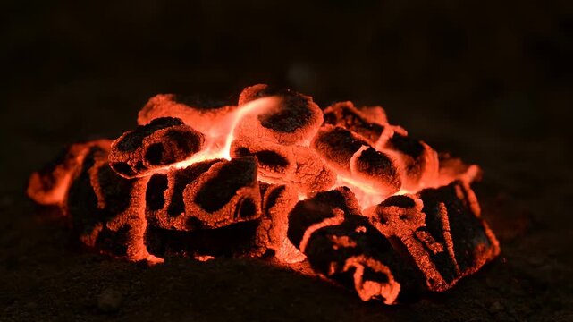 Glowing charcoal embers smolder and flicker in a dark outdoor fire setting. Fire safety education, camping and outdoor recreation promotion, and heating and warmth campaigns.