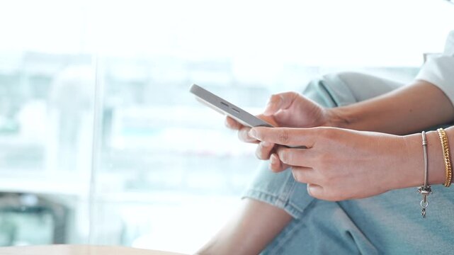 Woman using smartphone while sitting at cafe near glass window, typing and browsing on mobile phone with blurred passing train outside, urban lifestyle, digital communication and leisure in city.