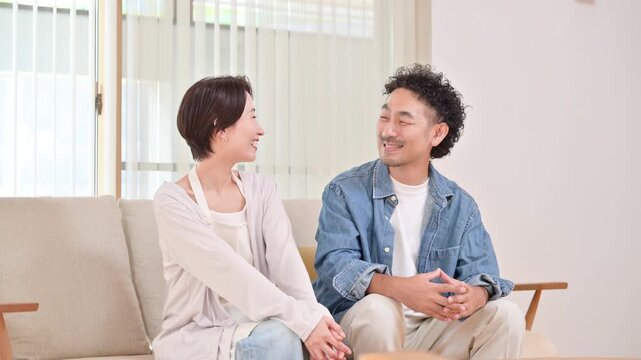 明るいリビングでくつろぐ会話する日本人夫婦、新築、マイホームのライフスタイルの笑顔イメージの動画