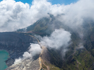 Vast volcanic crater breathes mist and smoke. Skyward clouds drift around jagged, rocky slopes at Mount Ijen © Cloudyew