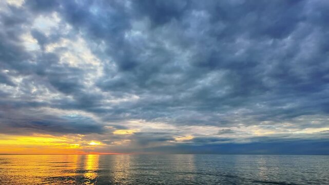 Timelapse of golden sunset over a calm sea with dark dramatic clouds moving across the sky.