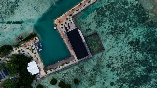 Aerial view of the pier and resort facilities on Pari island, surrounded by clear turquoise coral reef waters and sandy paths in South Kepulauan Seribu, Jakarta, Indonesia.