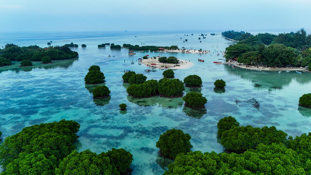 Aerial view of Pari island featuring lush mangrove forests, clear turquoise waters, sandy beaches, and small boats, South Kepulauan Seribu, Jakarta, Indonesia.