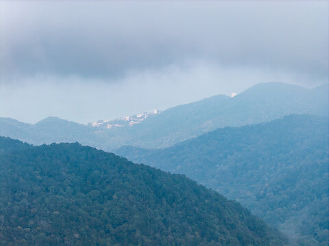 Misty mountains roll into depth with lush green peaks. Clouds loom low, softening distant ridgelines