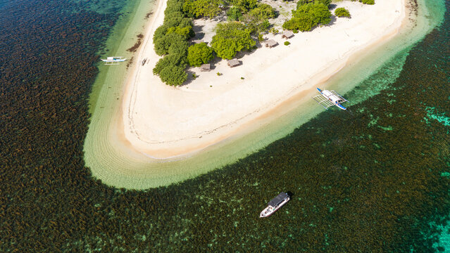 Aerial view of a tropical island with white sand beaches, lush trees, small huts, and traditional outrigger boats floating in clear turquoise water, Busuanga, Mimaropa, Philippines.