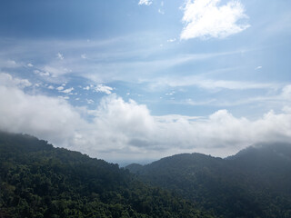 Misty clouds drift above lush green hills. Sunlight filters through scattered white clouds © Cloudyew