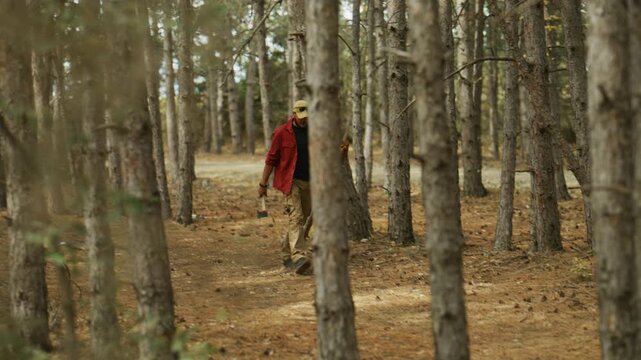 Lumberjack walks through a pine forest carrying an axe and firewood, illustrating bushcraft, survival skills and outdoor self-sufficiency.