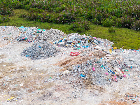 Piles of trash litter a barren, sunlit field. Plastic, glass, and metal scraps mix with discarded items