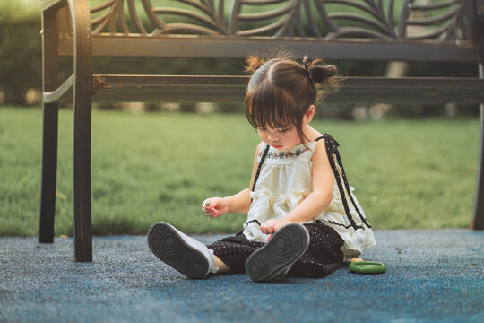 Curious toddler girl sitting outdoors and carefully examining small object in her hand with magnifying glass beside her, exploring nature through observation, discovery
