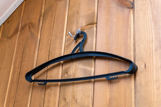 Close up of a simple black plastic coat hanger hanging on a metal hook on a natural timber wall panel