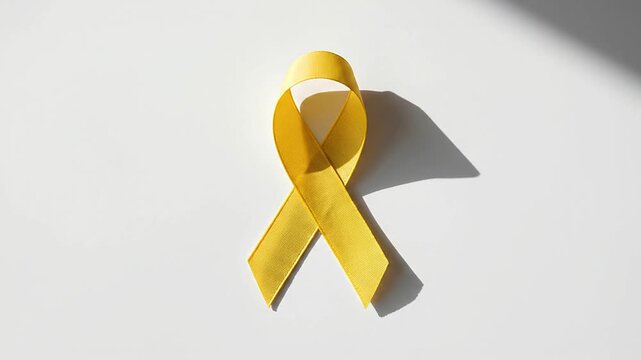 Yellow awareness ribbon symbol on white surface with shifting shadows