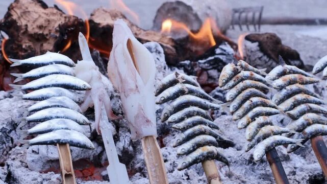 Rows of sardine skewers cooking over an open flame on a beach grill