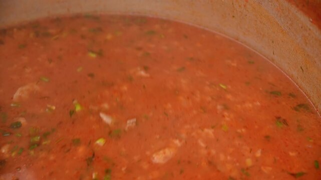 Gloved hand stirring hot red soup in a pot